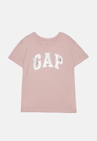 Lys rosa t-skjorte med korte ermer og rund hals, med en tykk, metallisk hvit "GAP" logo på forsiden i blokkbokstaver.