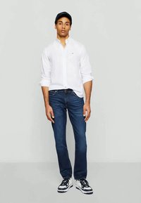 White button-up shirt, blue denim jeans, and black cap. Sneakers have white and black accents. Simple design suitable for casual wear.