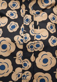 Μαύρο ύφασμα με μεγάλα μπεζ λουλούδια που έχουν μπλε κυκλικά κέντρα, με μια ραμμένη ραφή στη μέση.