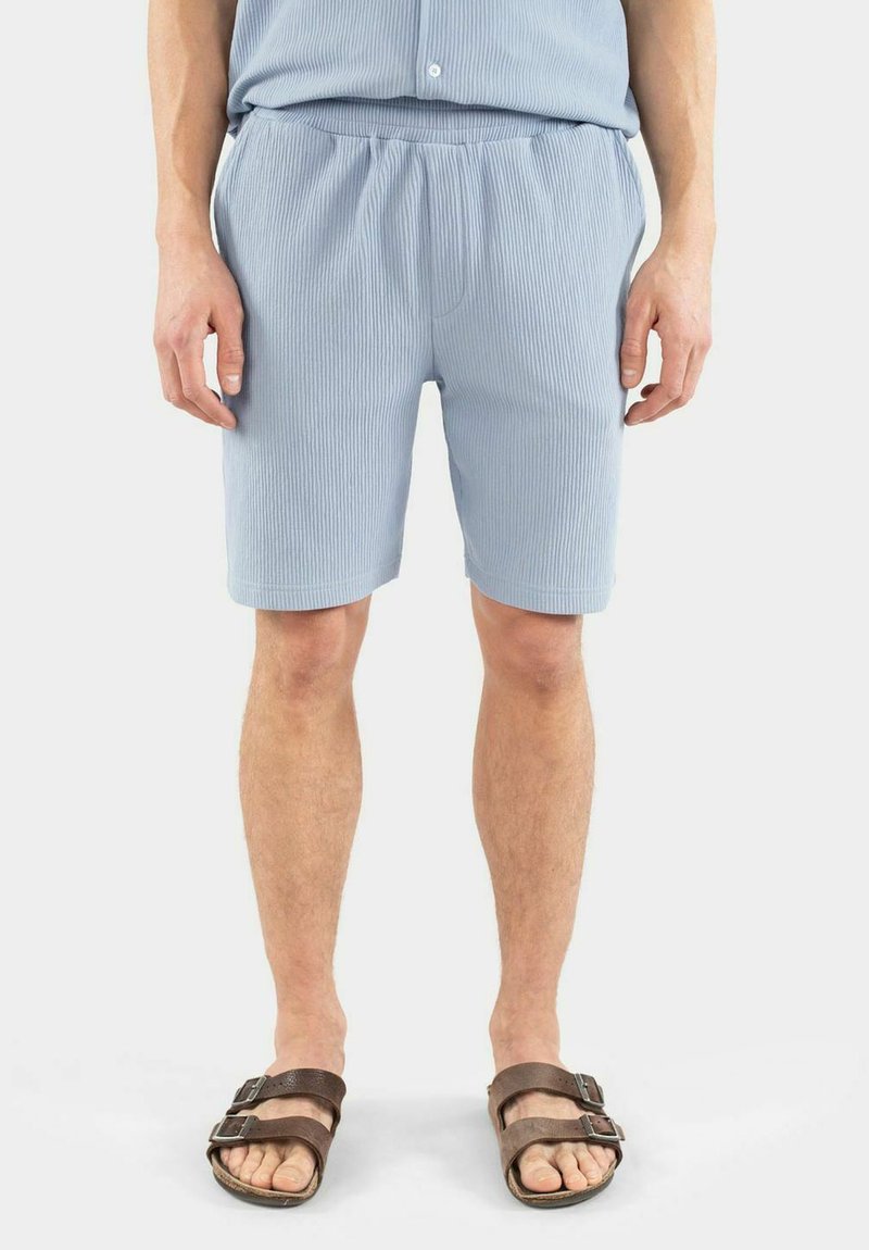 Ljust blå ribbade shorts med resårmidja, gjorda av ett mjukt tyg. Bärs med bruna sandaler med två justerbara remmar.