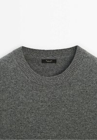Pull gris en maille à col rond avec col côtelé, montrant la partie supérieure de la poitrine et le décolleté.