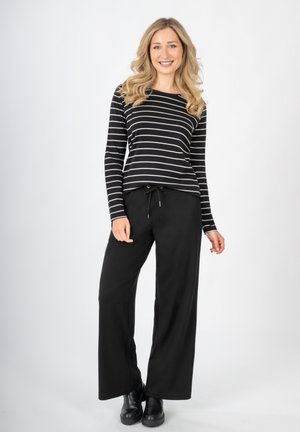Top a righe bianco e nero a maniche lunghe abbinato a pantaloni neri larghi, con vita regolabile. Modella che indossa stivaletti neri.