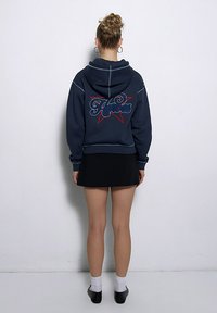 Granatowy hoodie z kieszenią typu kangur z przodu, haftowanym napisem "Bohaterowie" oraz wzorem gwiazdy. W połączeniu z czarną spódnicą i czarnymi butami.