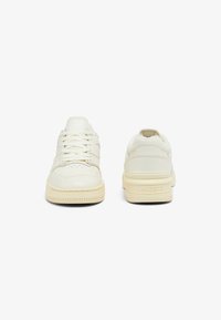Zapatillas bajas blancas de cuero con acentos texturizados, puntera redonda, cordones planos y detalle de logo en la parte trasera del talón.