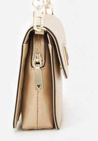 Beige syntetisk håndtaske med en tekstureret finish, guldfarvet hardware, lynlås lukning og en trekantet lynlåstrækker detalje.