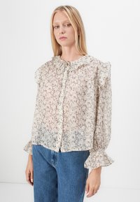 Blouse à motifs floraux en tissu léger et transparent. Dotée d'un col à volants, d'une fermeture à boutons et de manches évasées. Palette de couleurs douce.