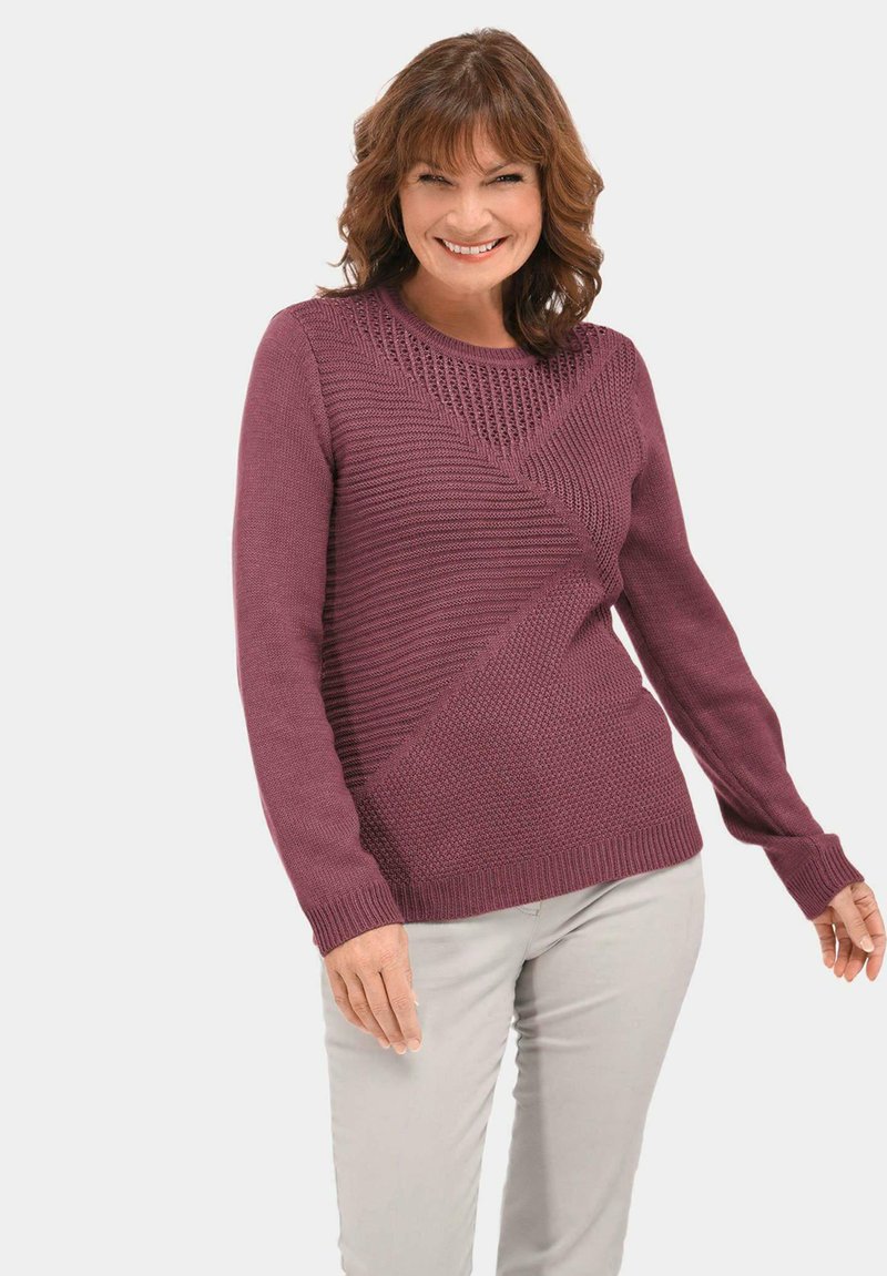 Bordeauxfarbener Strickpullover mit einem strukturierten diagonalen Muster, langen Ärmeln und einem gerippten Rundhalsausschnitt, kombiniert mit hellen Hosen.