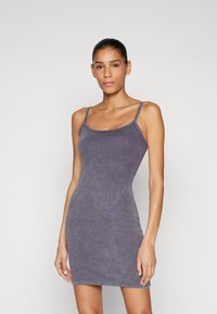 Purpurinė, prigludusi suknelė su plonomis petnešomis, pagaminta iš minkštos medžiagos. Turi subtilią tekstūrą ir tiesų apatinį kraštą. Nėra matomų raštų ar detalių.