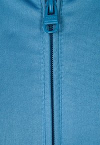 Světle modrá zipová bunda s texturovanou tkaninou, centrálním černým zipem a logem "Bench." na úchytu zipu.