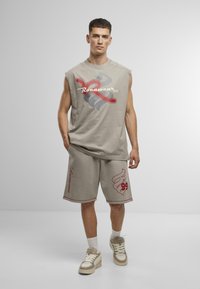 Beige ærmeløs top og shorts sæt med røde og grå grafiske designs. Materialet er blødt stof med en afslappet pasform, parret med lette sneakers.