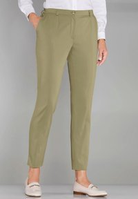 Khakifarbene, schmal zulaufende Hosen mit glatter Textur, Vorderfalten, Seitentaschen und Knopfschluss; kombiniert mit hellen, eleganten Schuhen.