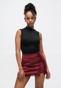 Top negro sin mangas con detalles fruncidos combinado con una minifalda burdeos con encaje en el borde y un diseño con volantes laterales.