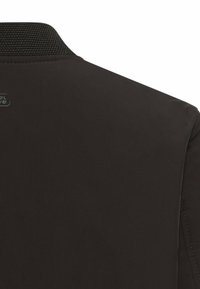 Sort jakke med en tekstureret krave, der har en glat overflade, subtile syningsdetaljer og et logo i nakken bagpå.