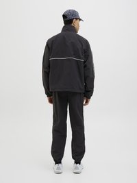 Black windbreaker jacket with a high collar and white piping, paired with matching trousers. White sneakers complete the outfit.