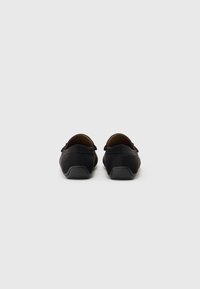 Zapatos de ante negros con parte trasera redondeada, acabado texturizado y suelas de goma bajas. Cuentan con un diseño tipo slip-on y mínimas decoraciones metálicas.