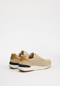 Zapatillas beige con un upper texturizado, detalles en cuero marrón claro y una suela azul oscura. Presentan perforaciones y un diseño de suela acolchada.