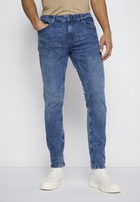 Jeans de mezclilla azul claro con un corte ajustado, que cuentan con bolsillos, cremallera y un ligero desvanecimiento. Combinados con zapatillas blancas de caña alta.