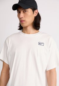 Hvid bomulds t-shirt med korte ærmer og rund halsudskæring, med et lille broderet marineblåt Nike-logo på brystet.