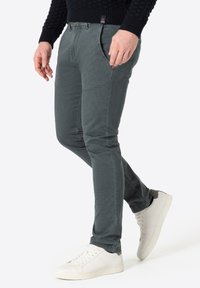 Graue Slim-Fit-Hosen aus einem strukturierten Stoff mit subtilen Fischgrätmuster. Mit Vordertaschen und braunen Knopfakzenten. Kombiniert mit weißen Sneakers.