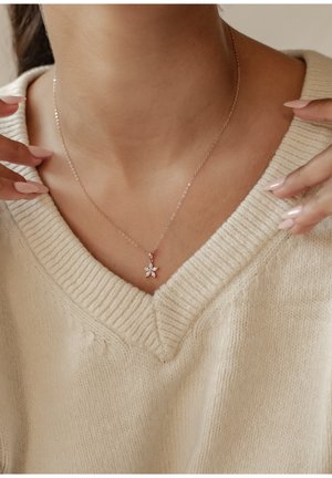 Zarte Halskette aus Roségold mit einem blumenförmigen Anhänger, der fünf blütenblattartige Elemente und einen subtilen Glanz aufweist, getragen über einem beigen Pullover.