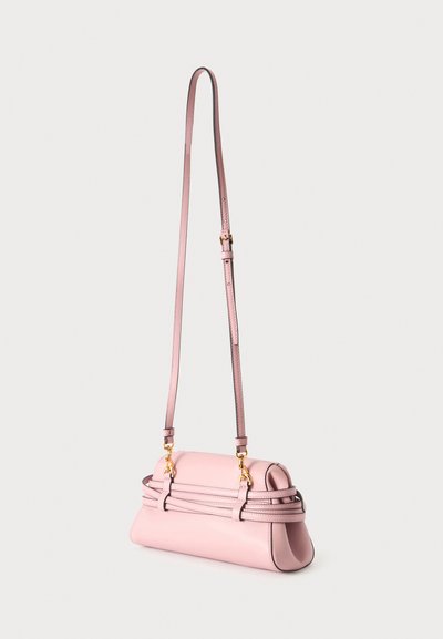 Sac à bandoulière en cuir rose clair avec une fine bandoulière réglable et des détails de boucle dorée sur un fond uni.