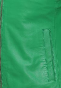 Groene leren jas close-up met een soepele textuur, horizontale rits en een klein rechthoekig zakje met stiksels.