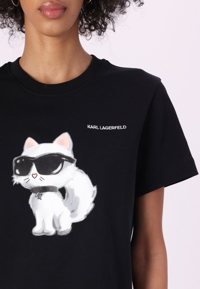 Черна памучна тениска с бяла карикатура на котка с очила, допълнена с текст "KARL LAGERFELD" в бяло. Къси ръкави, кръгло деколте.