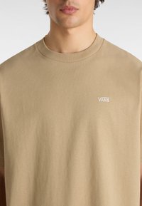 Beige cotton t-shirt featuring a crew neckline and a small, white embroidered "VANS" logo on the left chest. Smooth texture.
