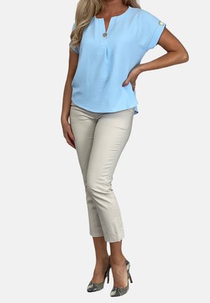 Hellblaue Bluse mit kurzen Ärmeln und Knopfdetail, kombiniert mit beigen, gekürzten Hosen und strukturierten, gemusterten High Heels.