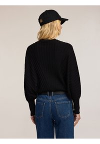 Maglione nero a coste con maniche lunghe e bombate, abbinato a jeans in denim blu a vita alta. Il maglione presenta un colletto rotondo e tessuto testurizzato.