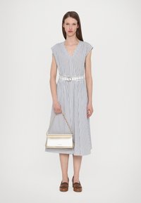 Robe rayée avec un décolleté en V et des manches courtes, cintrée à la taille avec une ceinture blanche. Associée à un sac à main doré métallisé et des chaussures marron.