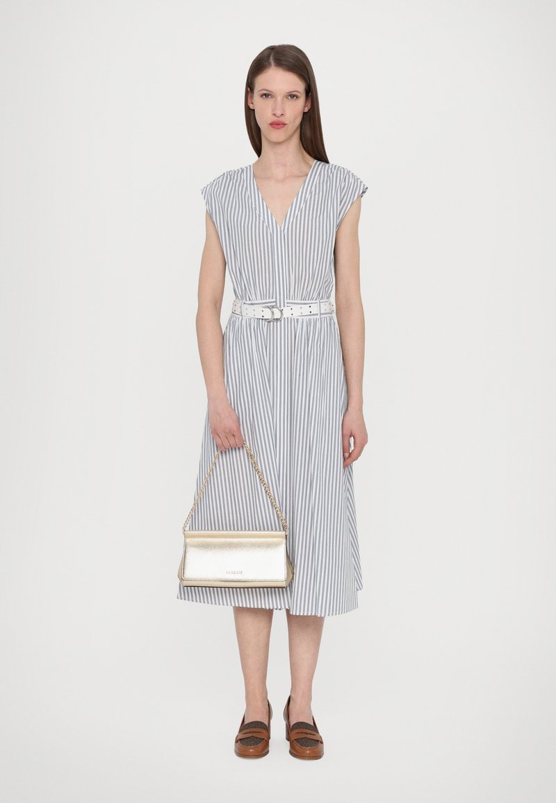 Robe rayée avec un décolleté en V et des manches courtes, cintrée à la taille avec une ceinture blanche. Associée à un sac à main doré métallisé et des chaussures marron.