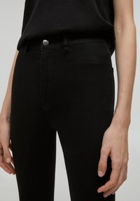 Black denim jeans featuring a slim fit, five-pocket design, and a metal button closure. The texture is smooth with minimal stitching details.