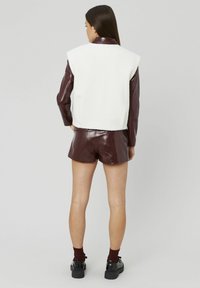 Gilet en polaire blanc, short en patent bordeaux court et chaussures noires épaisses. Le gilet présente un design structuré avec un col rond.