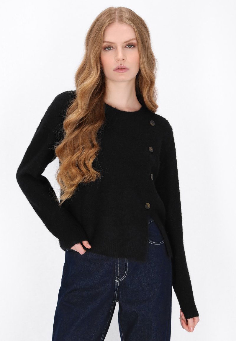 Sort strikket sweater med rund halsudskæring, der har fire brune knapper på venstre side. Lange ærmer og en let cropped pasform.