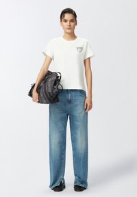 Camiseta blanca de manga corta con un pequeño diseño bordado, combinada con jeans sueltos de color azul claro y un bolso negro con un patrón y acentos multicolores.