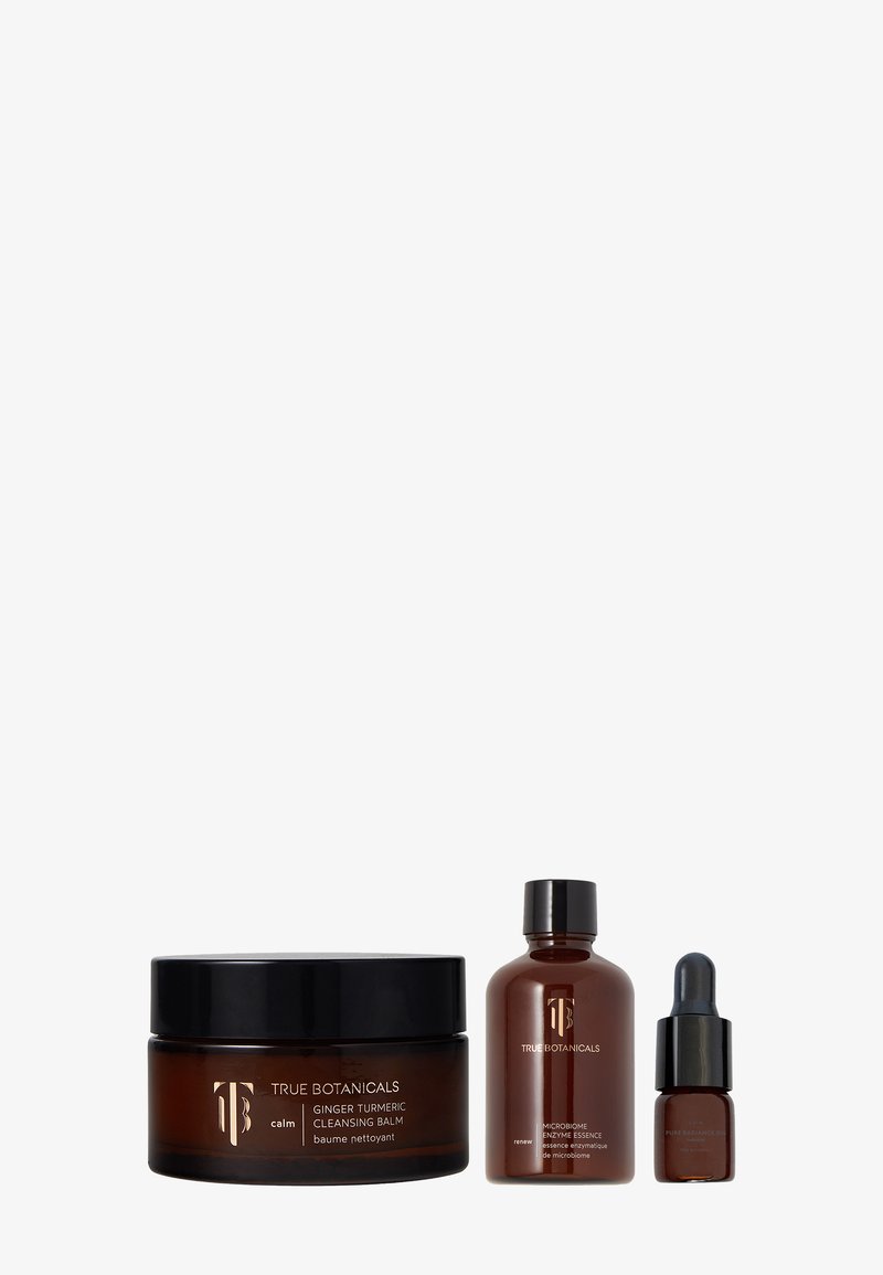 Drei Hautpflegeprodukte aus dunklem Bernsteinglas: ein runder Behälter für Reinigungsbalsam, eine schmale Flasche und eine Tropfflasche, alle beschriftet mit "True Botanicals".