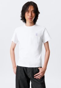White cotton t-shirt with short sleeves and a crew neckline. Features a small lavender bear logo on the upper left side.