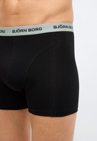 Άνδρας που φοράει μαύρα μποξεράκια Björn Borg με γκρι μέση και μαύρο λογότυπο σε απλό λευκό φόντο.