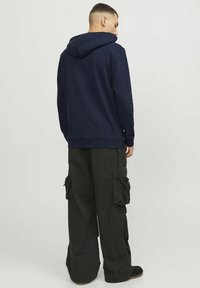 Sudadera azul marino con capucha ajustable, combinada con pantalones cargo negros de corte holgado que presentan bolsillos laterales y una textura en la tela.