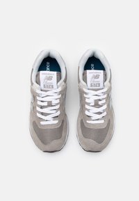 Šedé semišové a síťované tenisky s bílými tkaničkami a akcenty. Obsahují polstrovaný límec a jazyk, označeno "new balance Classic 574."