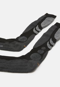 Svarta och grå strumpor med en texturerad mönstring som innehåller cirkulära och vågiga former, tillverkade av ett mjukt, elastiskt material.