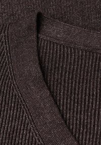 Nahaufnahme von dunkelbraunem, geripptem Strickstoff mit übereinandergelegten, gefalteten Kanten und strukturiertem Stich.