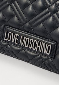 Svart kviltad läderyta med sydd mönster och metallplatta med "LOVE MOSCHINO"-logotyp fäst.