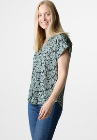 Blusa floreale verde menta con motivi floreali neri, maniche corte, placca con bottoni, vestibilità rilassata, realizzata in tessuto leggero.