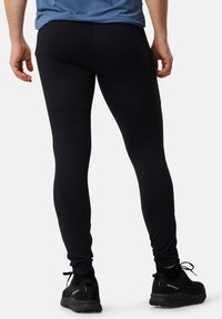 Schwarze Sportleggins mit eng anliegender Passform, gerippter Textur und Flachnaht. Tragen von schwarzen Turnschuhen mit Netzpaneelen und Schnürsenkeln.