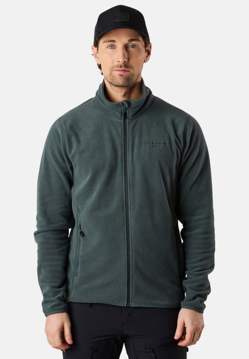 Vihreä fleece-takki, jossa on vetoketju etuosa, korkea kaulus ja kaksi sivutaskua. Sisältää hienovaraisen logon rinnassa. Sujuva tekstuuri.