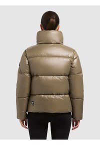 Pikowana oliwkowo-zielona kurtka puchowa z wysokim kołnierzem, teksturą pikowania oraz czarną metką z logo marki na dolnej prawej stronie.