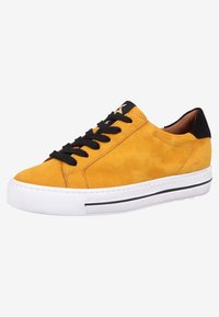 Baskets en daim jaune avec lacets et accent au talon noirs, semelle en caoutchouc blanche présentant une surface texturée et un détail de fine bande noire.