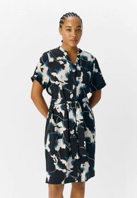 Robe noire à manches courtes, boutonnière à l'avant et ceinture à nouer, présentant un motif floral abstrait bleu et blanc sur un tissu texturé.
